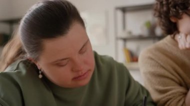 Down sendromlu bir kız, masa başında oturmuş origami tilkisi suratını çizerken renkli kağıtlara resim çiziyor.