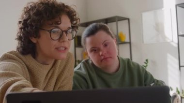 Down sendromu olan öğrencilere bilgisayar ekranında bilgi veren kadın öğretmen dikkatle dinliyor ve evde ders sırasında notlar alıyor.