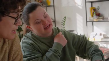 Down sendromlu bir kız, özel ders sırasında özel ders sırasında evde ders çalışırken deftere notlar yazıyor.