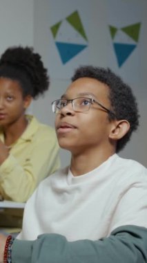 Sınıfta masa başında oturan Afrikalı Amerikalı çocuğun dikey görüntüsü. Ders sırasında sinema dışı öğretmeniyle sohbet ediyor.