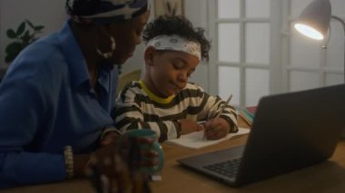 Afrika kökenli Amerikalı anne ve oğlunun evde eğitim görürken dizüstü bilgisayar kullanarak online iş yapmasının el kamerası görüntüsü.