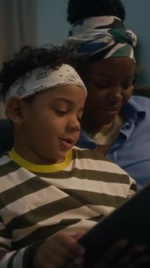 Siyahi kadının oğlunun yanında oturup evde eğitim sırasında şiir öğrendiği dikey bir fotoğraf.