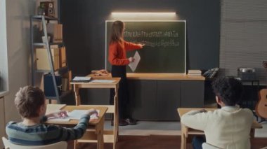 Müzik sınıfında karatahtaya yazılmış notlara işaret eden ve soru soran genç bayan öğretmen, sonra dört öğrenci sıralarında oturup cevap vermeye hazır.