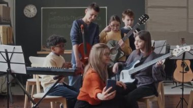 Okuldaki müzik dersinden sonra müzik enstrümanları tutan beş çoklu etnik öğrenciyle selfie çeken genç bayan öğretmen.