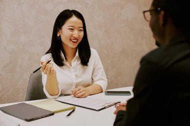Dost canlısı genç Asyalı İK yöneticisi tanınmayan siyahi adayla görüşürken gülümsüyor.