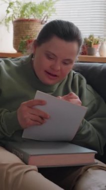 Down sendromlu çalışkan bir öğrencinin oturma odasında kanepede oturup ödevlerini yaparken not aldığı dikey bir fotoğraf.