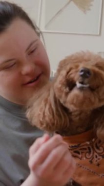 Down sendromlu bir kızın sevimli köpeğe ödül verirken ve evde onu hayranlıkla okşarken dikey pozu.