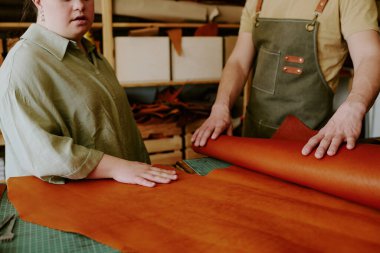 Unrecognizable man and woman with down syndrome touching natural leather while choosing material to sew leather bag clipart