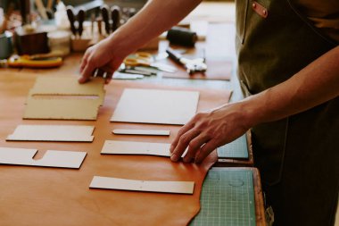 Tanımlanamayan erkek elleri süt rengi deri parçalarının üzerine ahşap şekiller seriyor. Gelecekteki detayları kesmek için.