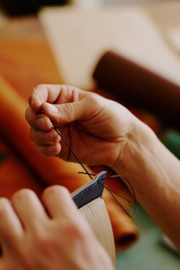 Tanımlanamayan erkek elleri deri dikiş dikmek için siyah iplikle büyük bir iğne tutuyor.