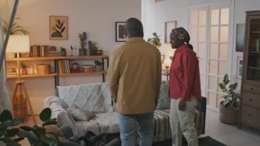 Afro-Amerikalı genç çift oturma odasına giriyor, el ele tutuşuyorlar, etrafa bakınıyorlar, kanepeye oturuyorlar, sonra da hevesle yeni daireleri hakkında konuşuyorlar.