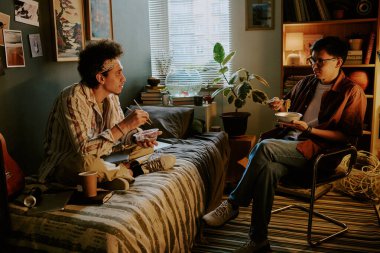 Çift ırklı oda arkadaşları Çin yemeği yiyor ve yurt odalarında sohbet ediyorlar.