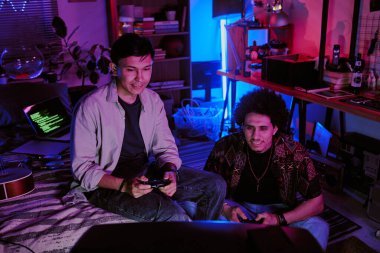 Elektronik cihazlarla dolu neon bir odada TV 'de kümes oyunu oynarken ellerinde oyun platformu tutan kardeşler.