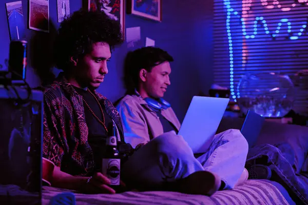 stock image Focused roomies sitting on single bed and drinking beer while working on joint IT project