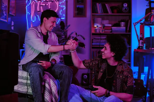 İki adam retro yurt odasında oyun üstüne el sıkışıyor.