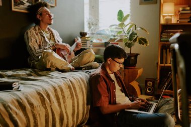 İki öğrenci arkadaş evde oturup gitar çalmak ve bilgisayar oyunu oynamak gibi şeyler yapıyorlar.