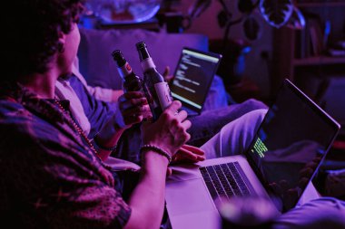 Unrecognizable men celebrating with bottles of beer working code launched on their laptops clipart