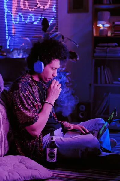 stock image Curly-haired developer taking inhalation of sweet vape while checking codes on laptop