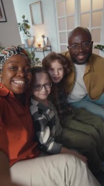 Sosyal medya için selfie videosu çekerken iki beyaz çocuğun ve Afrikalı Amerikalı ailelerin kameraya el sallamalarının dikey görüntüsü.