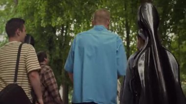 Genç markaların ve bayan sokak müzisyenlerinin arka plandaki manzarası yaz günü parkta müzik aletleriyle yürümeleri.