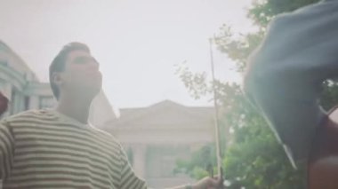 Genç vibey 'in kemanını tutarken ve gözleri kapalı dans ederken arkadaşının güneşli yaz gününde dışarıda çaldığı çello müziğinin keyfini çıkarırken.