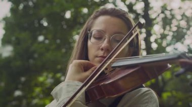 Genç bir kadının yayla keman çaldığı ve dışarıda parkta telleri ayarladığı sahneyi çek.