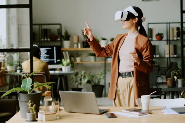 VR kulaklık takan genç Asyalı kadın geliştirici BT şirketinin önde gelen ofisinde biyofilik tasarım ile sanal uygulamayı test ediyor.