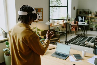 Genç Afrikalı Amerikalı erkek programcının modern bilişim şirketinde VR kulaklık kullanırken yüksek açılı görüntüsü.