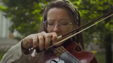 Genç ve yetenekli bayan müzisyen parkta şarkı söylerken keman çalıyor.