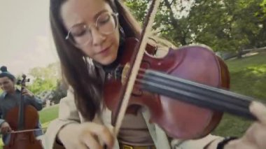 Genç bayan müzisyenin parkta koro eşliğinde keman çalarken görüntüsü Hollanda açılı.