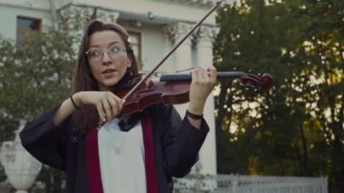 Genç bayan müzisyen yavaşça keman çalıyor, sonra parkta dışavurumcu açık hava konserinde hızlı geçiş yapıyor.