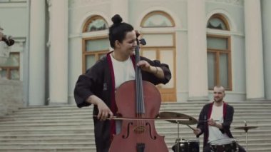 Parktaki performans sırasında tarihi konağın önünde çello, keman ve davul çalan bir grup profesyonel müzisyen