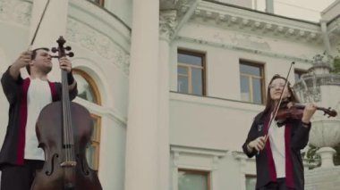 Tarihi binanın önündeki merdivenlerde çello çalıp çello çalan bir grup sanatçı parktaki konser sırasında insanları eğlendiriyorlar.