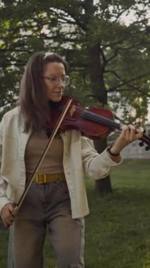 Yaz günü parkta canlı müzik eşliğinde keman çalan genç sanatçı kadın müzisyenin dikey çekimi.