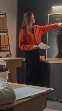 Kadın öğretmenin müzik dersi sırasında tahtada durup soru sorduğu dikey çekim. Küçük çocuk cevap vermek için elini kaldırıyor.