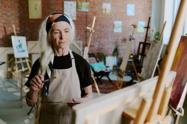 Modern son sınıf beyaz kadın palet tutuyor ve resim stüdyosunda tuval üzerinde boya fırçası resmi yapıyor.