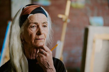 Kafkasyalı üst düzey kadın ressamın, elinde kalemle tuvaldeki çizime bakıp, boşluğu kopyaladığı yakın plan.