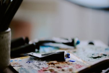 Sanatçı işyerindeki paletlerin üzerinde duran açık akrilik ya da yağ boyası tüplerinin yakınlaştırılması