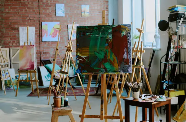 Modern sanat stüdyosunun iç mekânında resim çeken insanlar yok. Tablo üzerinde soyut akrilik resim olan, uzayı kopyalayan.