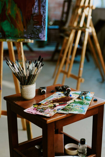 Вертикальный кадр из набора кистей, краски трубки, палитры на небольшом деревянном столе в современной художественной студии или школе