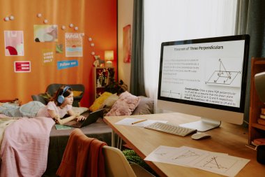 Gençler odasında matematik dersi olan masaüstü bilgisayarı, arka planda dizüstü bilgisayarda sörf yapan kız.