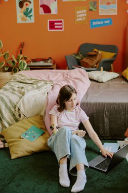 Özürlü bir gencin rahat yatak odasında yerde oturup laptopla çalışıp, boşluğu kopyaladığı dikey bir fotoğraf.