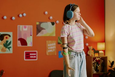 Kol protezi takmış, kulaklıkla gözleri kapalı müzik dinleyen orta boy alfa bir kız.