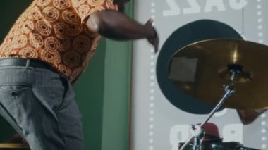 Konga davulu Afrikalı bir adam müzik stüdyosuna giriyor, grup arkadaşını el sıkışarak ve kucaklayarak selamlıyor, sonra da provaya başlamak için yerini alıyor.