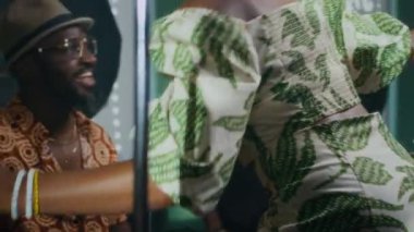 Gülümseyen Afrikalı genç caz şarkıcısı müzik stüdyosuna giriyor, erkek grup arkadaşlarını yanaktan öpücükle selamlıyor ve mikrofon yerleştiriyor.