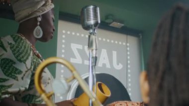 Neşeli Afrikalı Amerikalı genç vokalist. Mikrofonun önünde durup prova sırasında iki erkek grup arkadaşıyla konuşuyor. Sonra da şarkı söylemeye başlıyor.