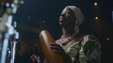 Zenci genç bir kadın müzik stüdyosunda Guiro çalıyor ve şarkı söylüyor.