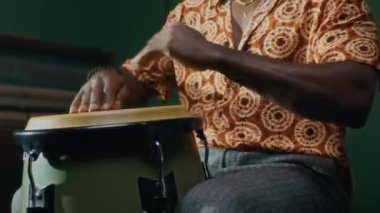 Müzik stüdyosunda elleri ile konga davulu çalarken odaklanmış siyahi bir adamın ritm kompozisyonu yaratma görüntüsü.