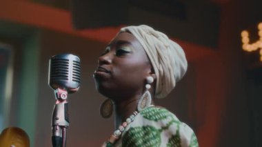 Mikrofonun önünde şarkı söyleyen ve barda Guiro çalan Afro-Amerikan genç kadını yakından izleyin.