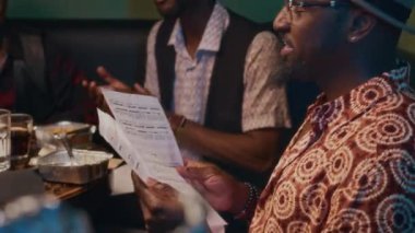 Gösteriden önce barda yemek yiyen dört Afrikalı Amerikalı caz müzisyeni, elinde notalı kağıtlar tutan bir adam.